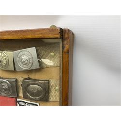 Display of eleven German belt buckles including 'SS', Party Buckle, two Army, Fire Service, two Luftwaffe, NSKK, Hitler Youth and WW1 Army; framed with three cloth badges and an armband