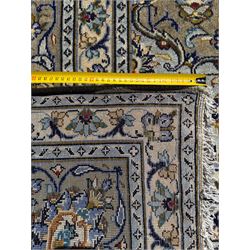 Central Persian Kashan pale khaki and ivory ground carpet, shaped central medallion enclosing small stylised motifs, the field decorated profusely with trailing foliate branches and plant motifs, guarded border with repeating floral design
