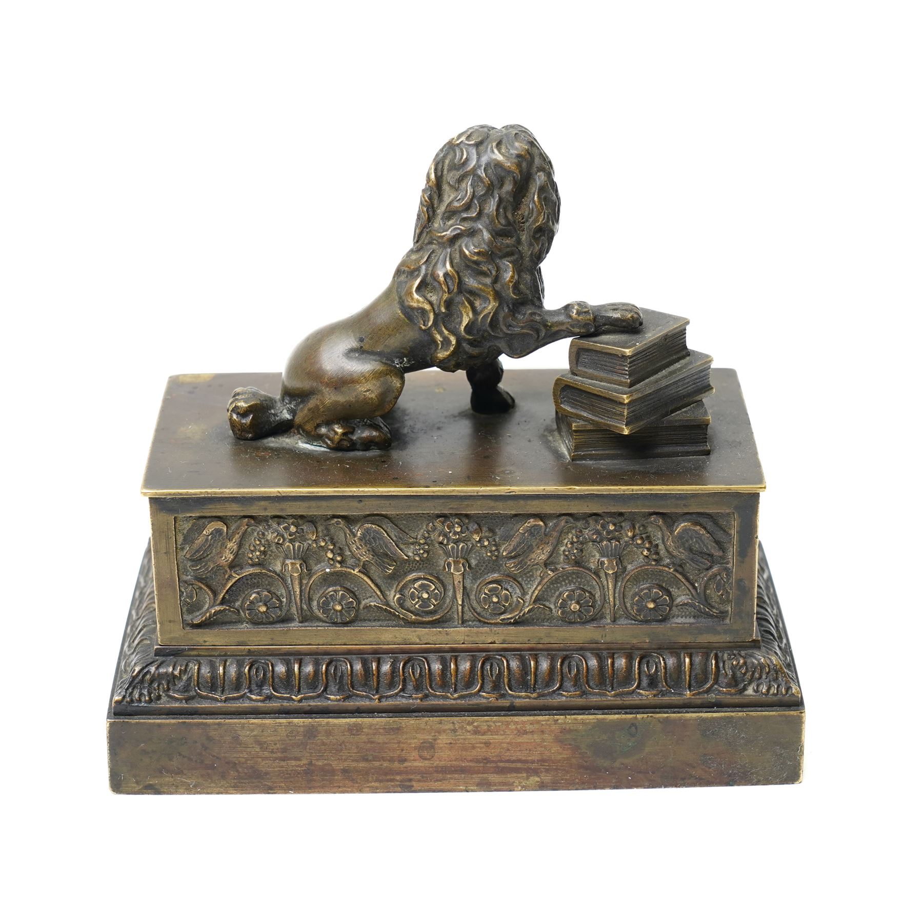 19th-century Grand Tour patinated bronze inkwell, surmounted by a recumbent lion, the beast modelled in the antique manner with one paw resting upon a stack of books, emblematic of strength, learning and guardianship. The stepped rectangular base cast with classical foliate friezes, fitted with multiple apertures and an inset ceramic inkwell and pounce pot; an erudite decorative object in the Grand Tour tradition, drawing on Renaissance and Roman prototypes, W12.5cm H11.5cm