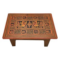 Late 20th century Burmese low table, the rectangular top and frieze decorated in traditional Shwezawa lacquer with gilded celestial figures, mythological beasts and dense foliate scrollwork, the folding base with hinged slab supports bearing conforming decoration