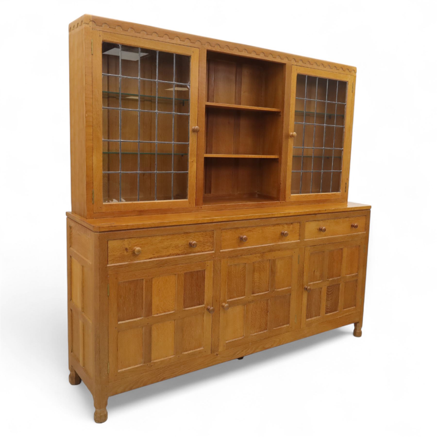 David 'Oakleafman' Langstaff - oak three drawer dresser, the scalloped cornice above a back with central open shelves flanked by two glazed and leaded cupboard doors opening to glass shelves, upon a base with adzed top carved with signature leaf, three drawers and three panelled cupboard doors with turned handles, upon octagonal feet, from the workshop of David Langstaff, Easingwold, Yorkshire