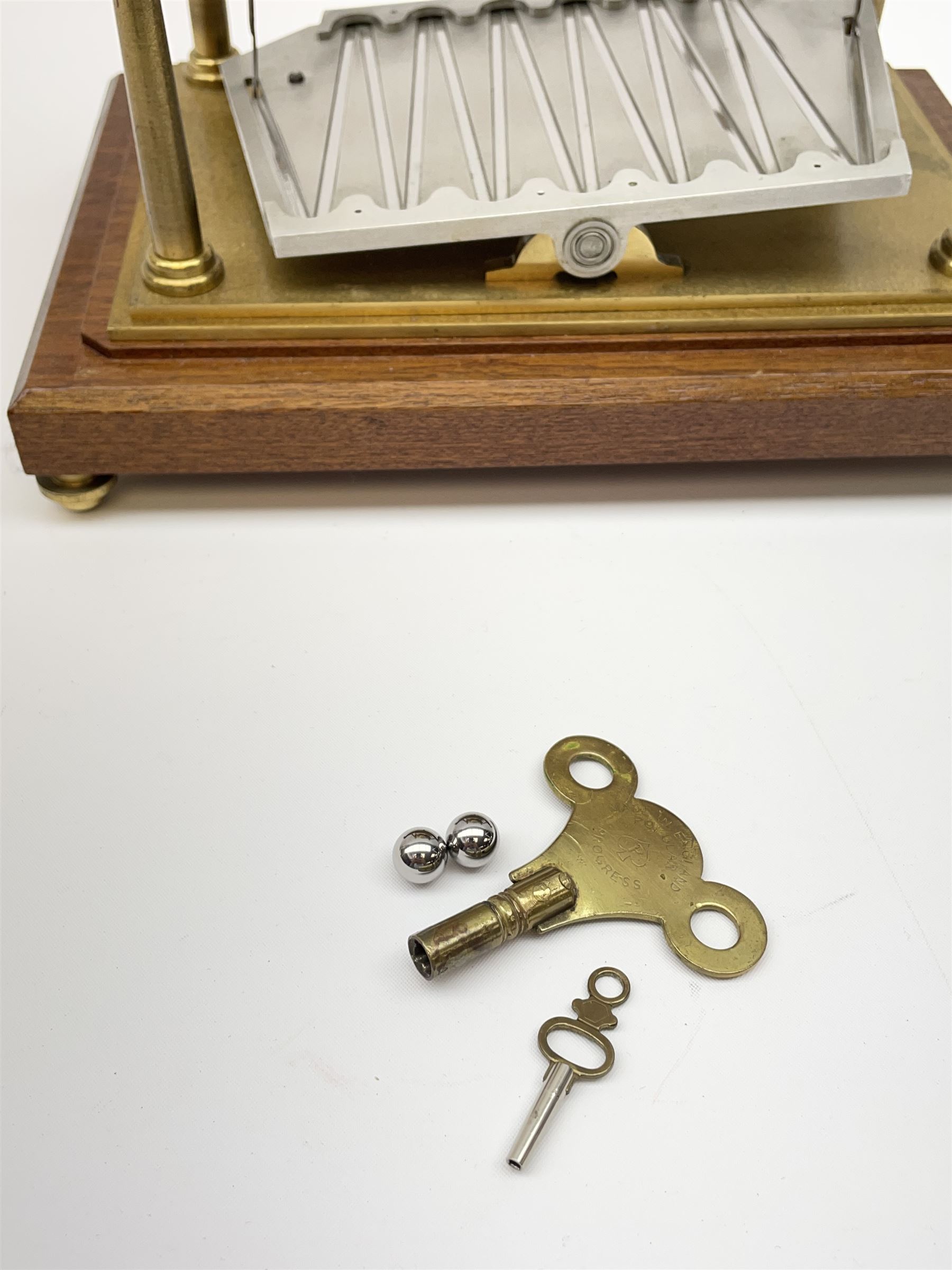 Mid 20th century 'Congreve' rolling ball clock, sloped arch and pierced brass movement, the central Arabic minute chapter ring flanked by hour and seconds dials, twin train driven eight day movement, raised on mahogany plinth with turned brass feet, under acrylic cover