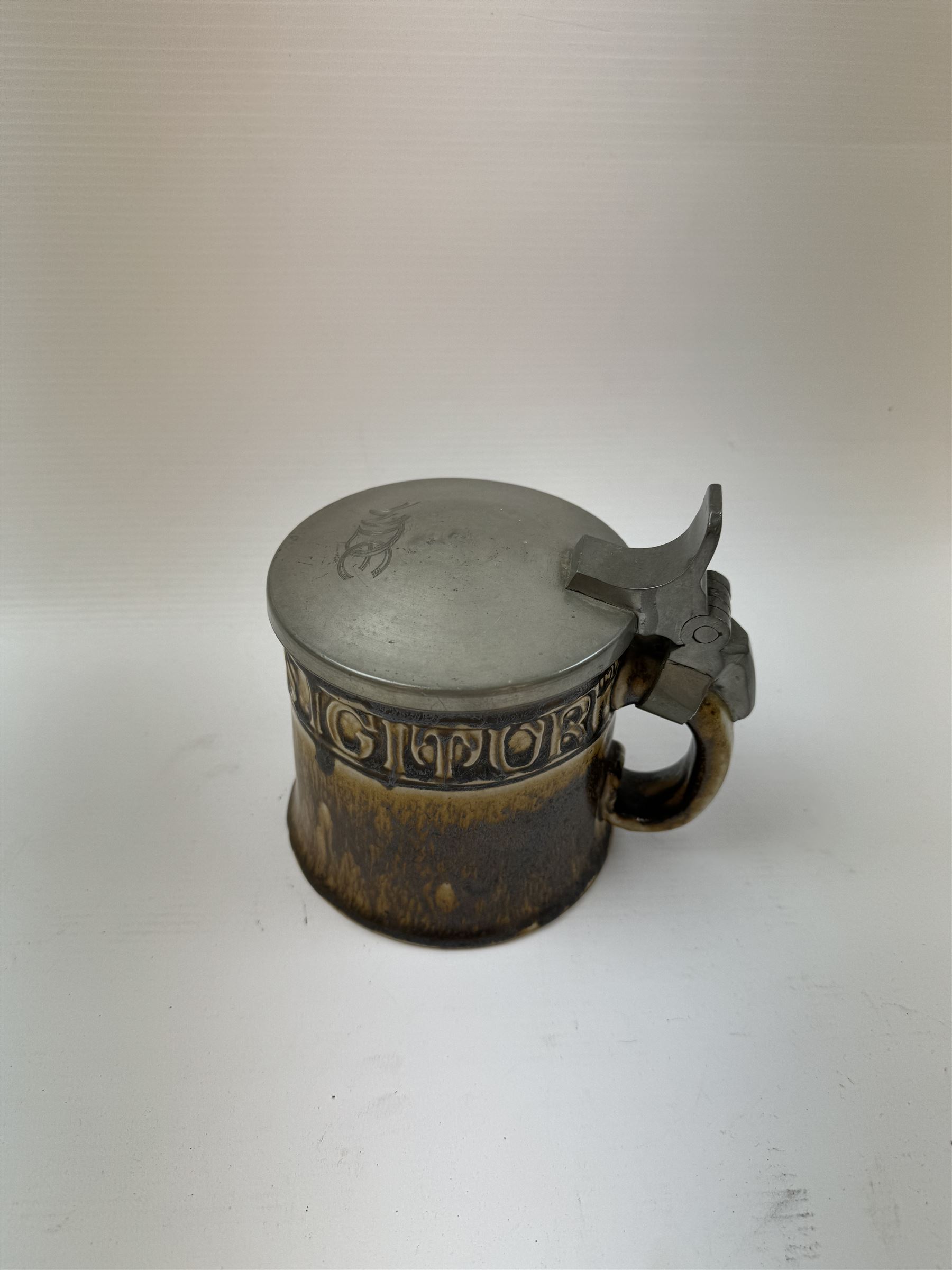 Arts and Crafts or Jugendstil tankard by Richard Riemerschmid, circa 1906, the cylindrical stoneware body reading 'Gaudeamus Igitur' (therefore let us rejoice), and finished in a brown glaze, with engraved slightly domed hinged lid, impressed mark beneath for Reinhold Merkelbach Grenzhausen, model number 2026 W, H14.5cm 