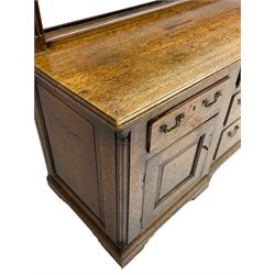 George III oak dresser, projecting dentil cornice over three heights plate rack enclosed by fluted uprights, the dresser fitted with five drawers and two panelled cupboards, canted corners with fluted quarter columns, on bracket feet