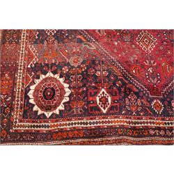 Large Persian Shiraz crimson ground carpet, the busy field decorated with a geometric pole medallion surrounded by stylised plant motifs with contrasting indigo spandrels and geometric-woven guard bands