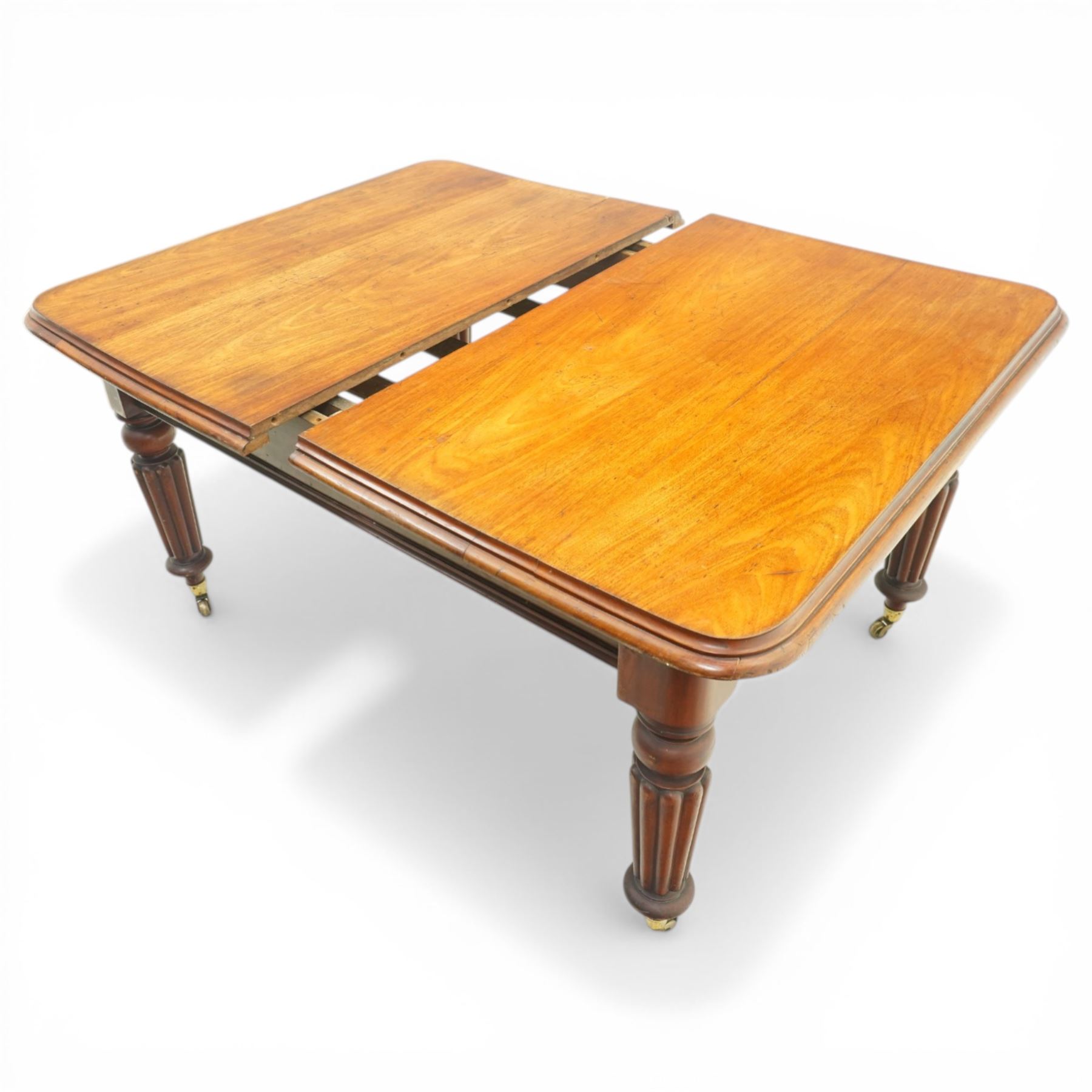 Victorian mahogany extending dining table, rounded rectangular top with moulded edge and two additional leaves, on four turned and fluted supports with brass caps and castors, extension mechanism beneath, in need of restoration