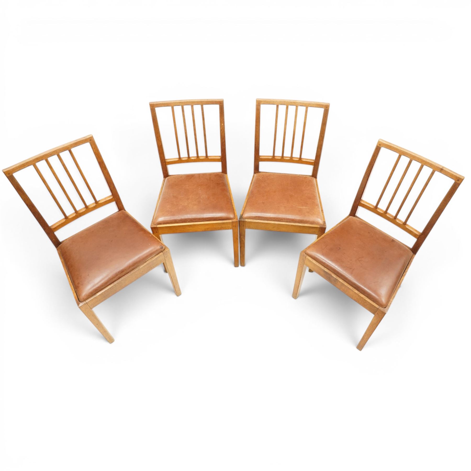 Acornman - set of four oak dining chairs, chamfered slatted back, tan leather drop in seat, raised on square supports with carved acorn signature, by the workshop of Alan Grainger of Brandsby