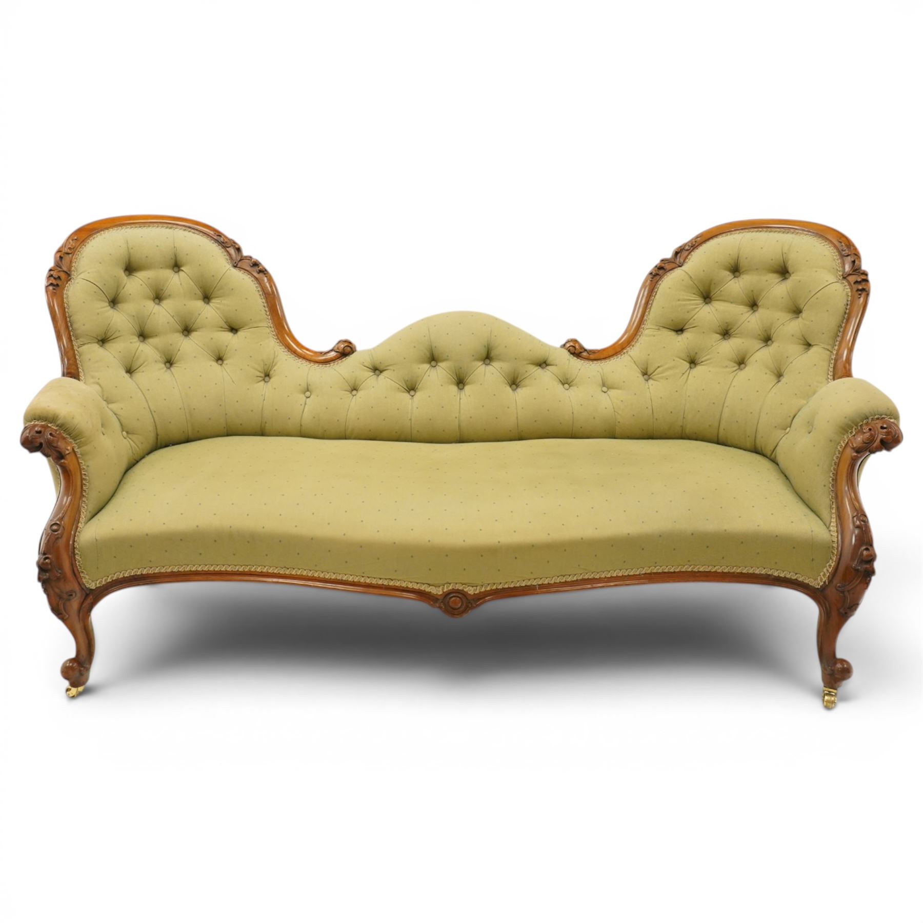 Victorian mahogany framed double ended chaise longue, serpentine button upholstered back with raised scrolled ends, padded arms and stuff-over seat upholstered in green fabric, carved showframe with foliate terminals and scroll supports, on short cabriole legs with brass castors