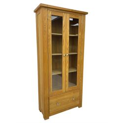 Light oak bookcase display cabinet, projecting square cornice over glazed double doors enclosing three adjustable shelves, single drawer base, on stile supports