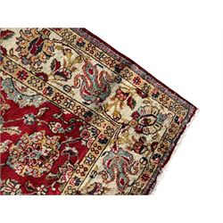 Persian Tabriz crimson ground rug, the field decorated with large palmette and stylised plant motifs connected by interlaced leafy branches, trailing border decorated with similar palmette motifs within floral pattern guard stripes, with signature panel 