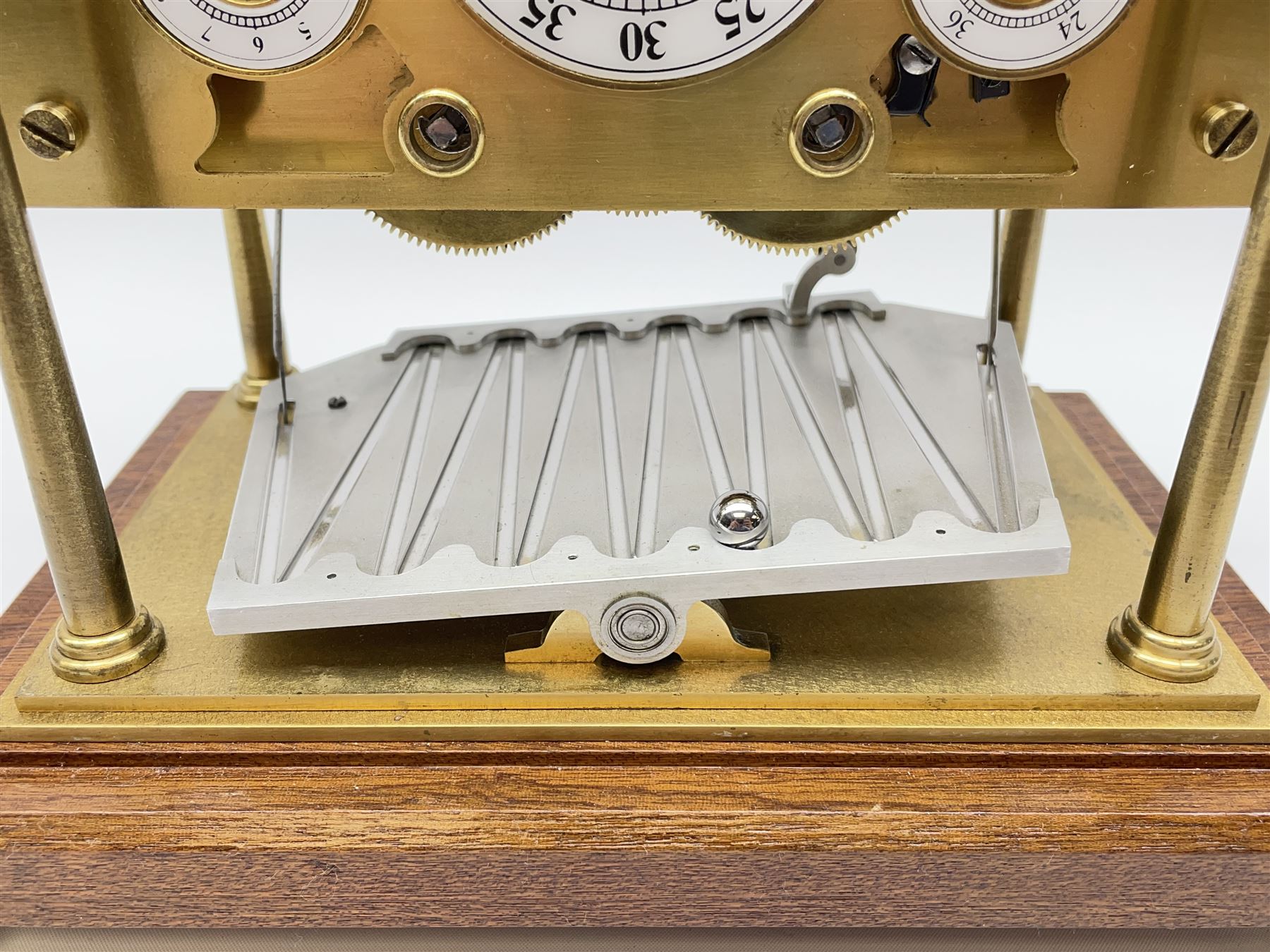 Mid 20th century 'Congreve' rolling ball clock, sloped arch and pierced brass movement, the central Arabic minute chapter ring flanked by hour and seconds dials, twin train driven eight day movement, raised on mahogany plinth with turned brass feet, under acrylic cover