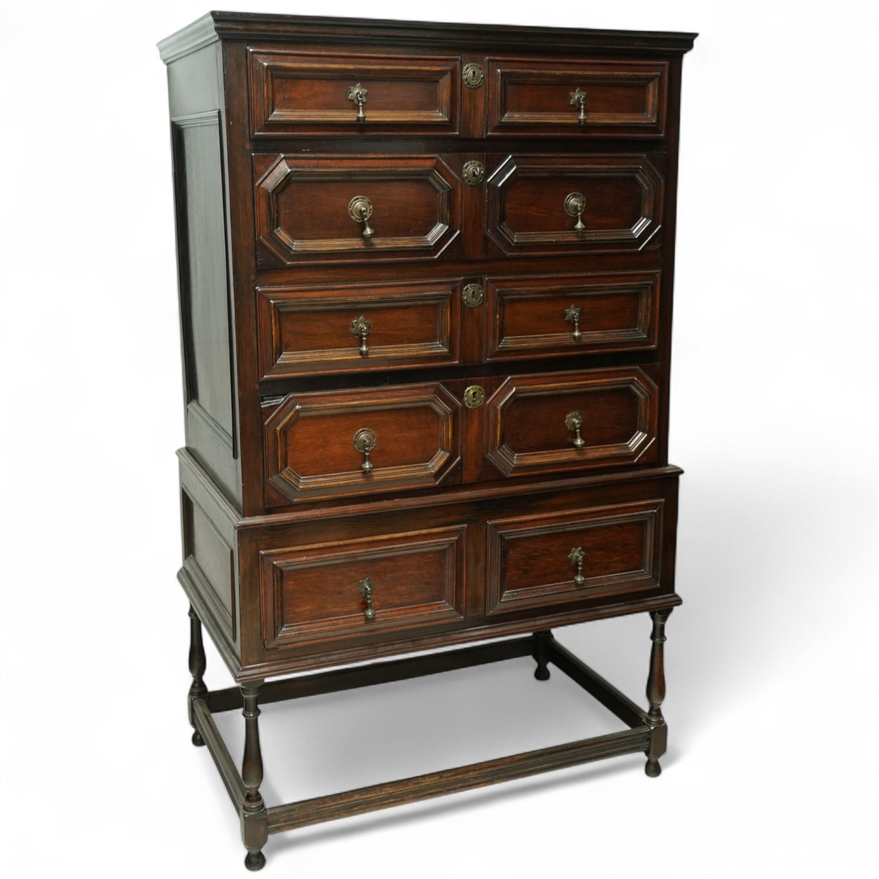 Jacobean style oak chest on stand, four full-length graduated drawers decorated with geometric mouldings, brass pear drop handles and escutcheon, the stand with two drawers above turned legs on a stretcher base on all sides, raised on pear-shaped feet, 18th century and later 

 