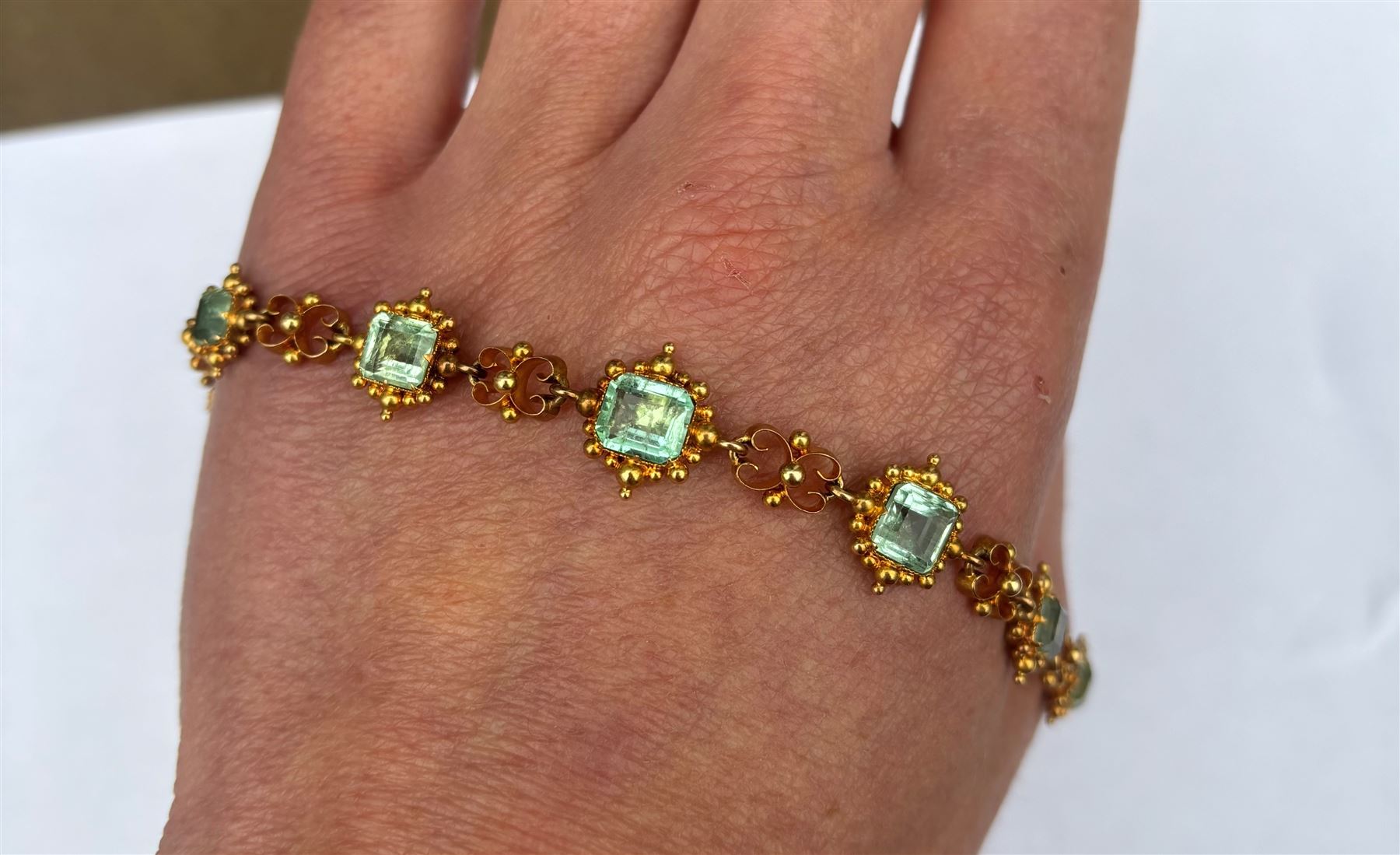 19th century gold emerald necklace, seven closed back octagonal cut and square cut emeralds, surrounded by a fancy bead setting, each spaced by a pierced scroll and bead design link, to a cable link chain necklace, with The Gem & Pearl Laboratory report