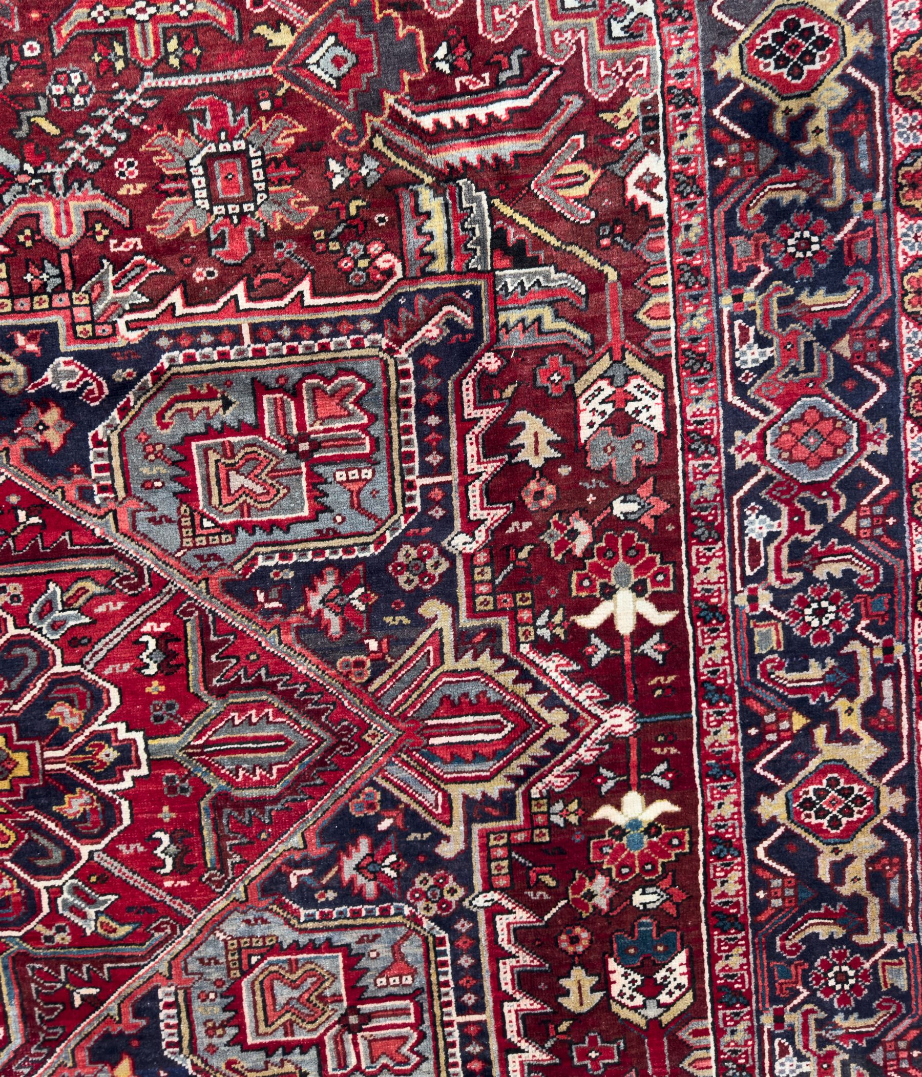Northwestern Persian Heriz carpet, the madder red field centred by a large octofoil medallion with serrated edge, flanked by ivory stepped spandrels and geometric floral motifs in indigo, ochre and sky blue, enclosed by a navy border of rosettes and angular vines, from the region of Heriz