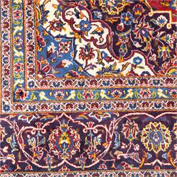 Central Persian Kashan hand-knotted carpet, crimson central field with lobbed medallion in navy blue and ivory ground, surrounded by a dense all-over floral design of scrolling vines, palmettes, and stylized blossoms, enclosed within a deep navy main border, flanked by multiple guard stripes with fringe ends 


