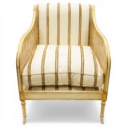 Louis XV design cream painted and parcel-gilt bergere armchair of large proportions, high scrolled back over canework arms, upholstered in striped fabric with over-stuffed loose seat cushion, on fluted supports