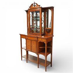 Edwardian Sheraton Revival inlaid mahogany breakfront cabinet, the broken swan neck pediment with central finial inlaid with cartouche and scrolling floral festoons, the central cabinet fitted with astragal-style glazed door with central urn and swag motif, flanked by arched bevelled mirrors over a shelf and gadrooned bracket over paterae inlays, base fitted with marquetry frieze rawer over a panelled cupboard with intricate inlaid scrolling floral designs, flanked by open shelves, raised on square tapering herringbone inlaid supports united by undertier