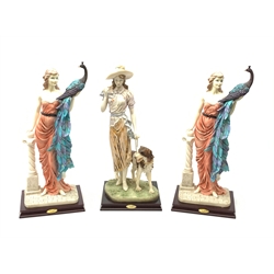  A pair of La Anina Collection figurines, each modelled as a female figure in pink dress supporting a peacock on one arm, and resting the other upon a classical column, H51.5cm, together with another similar figurine modelled as a female figure with hound at her side.   