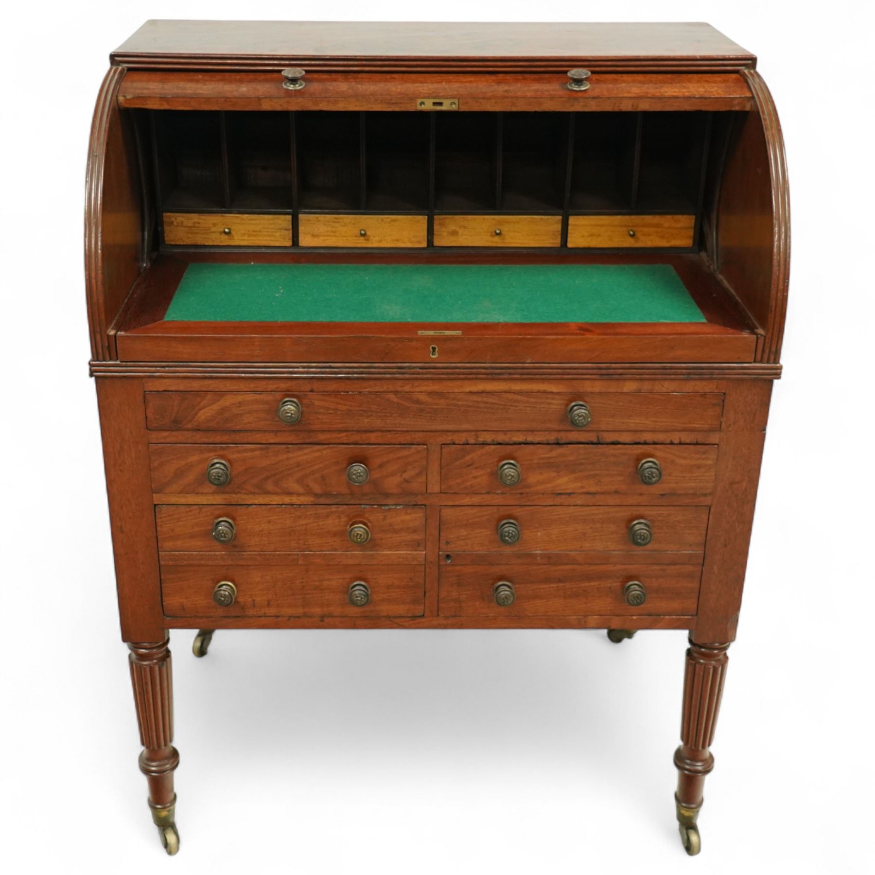 Regency period mahogany cylinder desk, the roll-top enclosing a fitted satinwood interior with pigeonholes and drawers, sliding green baize writing surface, lower section fitted with four drawers and a cupboard, on reeded tapering legs with brass caps and castors