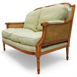French Empire design varnished wood three piece lounge suite comprising of two cane armchairs and matching sofa, carved top rails with foliate terminals, cane side panels and padded scroll arms, upholstered in a green brocade with matching piping, on fluted legs