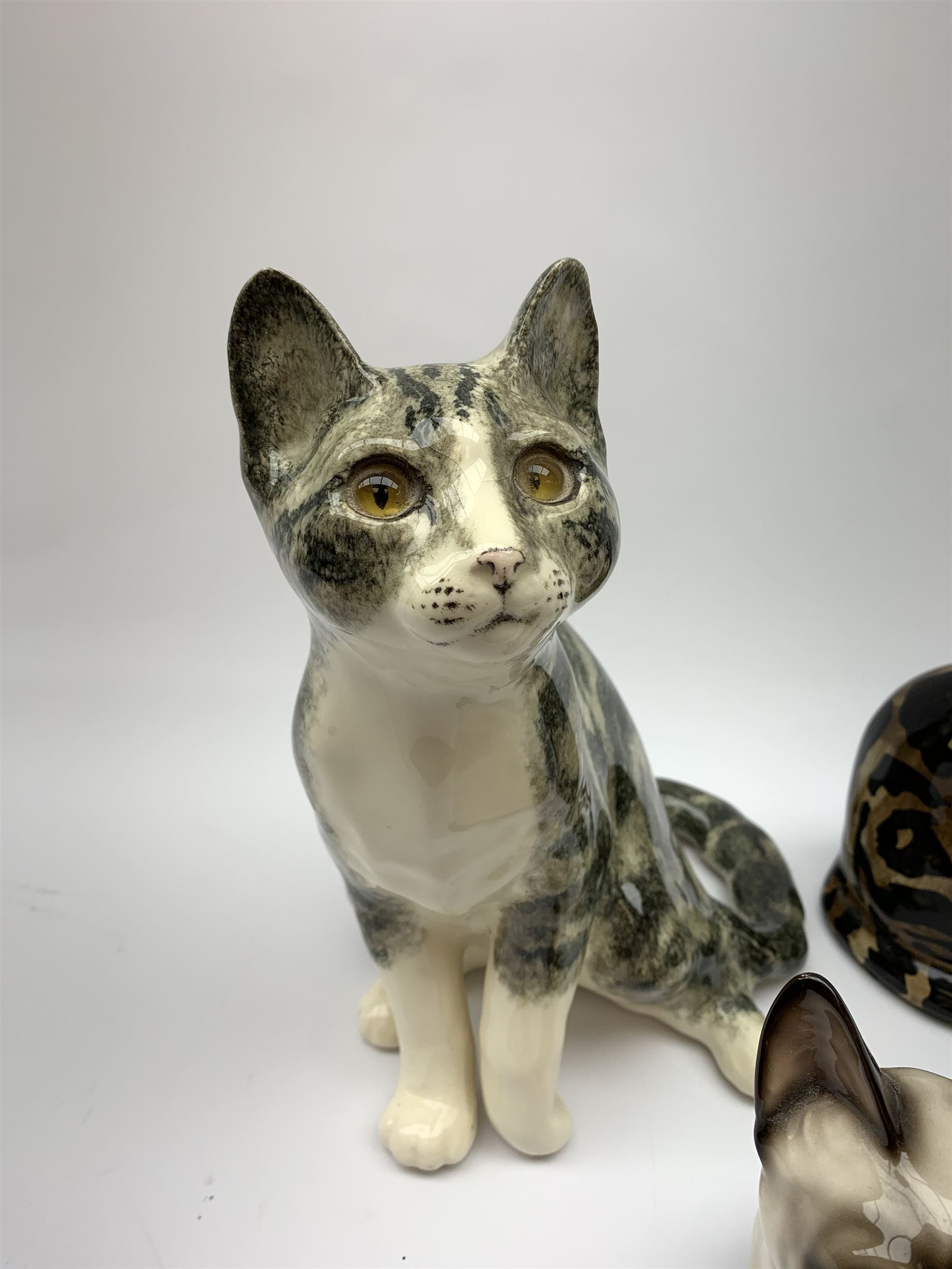 A Winstanley cat, with glass eyes in seated post, signed beneath, H25cm, together with three other figures of cats, including a Rye Pottery example. (4). 