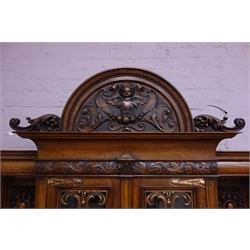  Edwardian oak sideboard, carved pediment with winged cherub, stepped projecting cornice, carved foliate frieze, above two glazed doors with copper work, flanked by turned and fluted columns, three ogee front drawers, two cupboards with carved mask, pointed ogee arch with egg and dart, two turned columns with acanthus carvings, projecting plinth base on bun feet, W213cm, H238cm, D73cm  