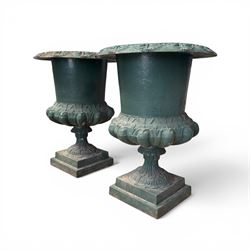 Pair of Victorian cast iron campana garden urns, the flared rim with repeating stylised anthemion motifs with scrollwork, over a deep gadrooned and Aesthetic moulded underbelly, fluted and foliate lower bowls on square pedestal bases, in antique green-painted finish