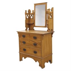 Edwardian stained pine dressing chest, the moulded top over three graduating drawers with pressed brass handles, shaped apron and bracket feet, the mirror back with rectangular plate on pivot supports, flanked by pierced Gothic style uprights with small corner shelves