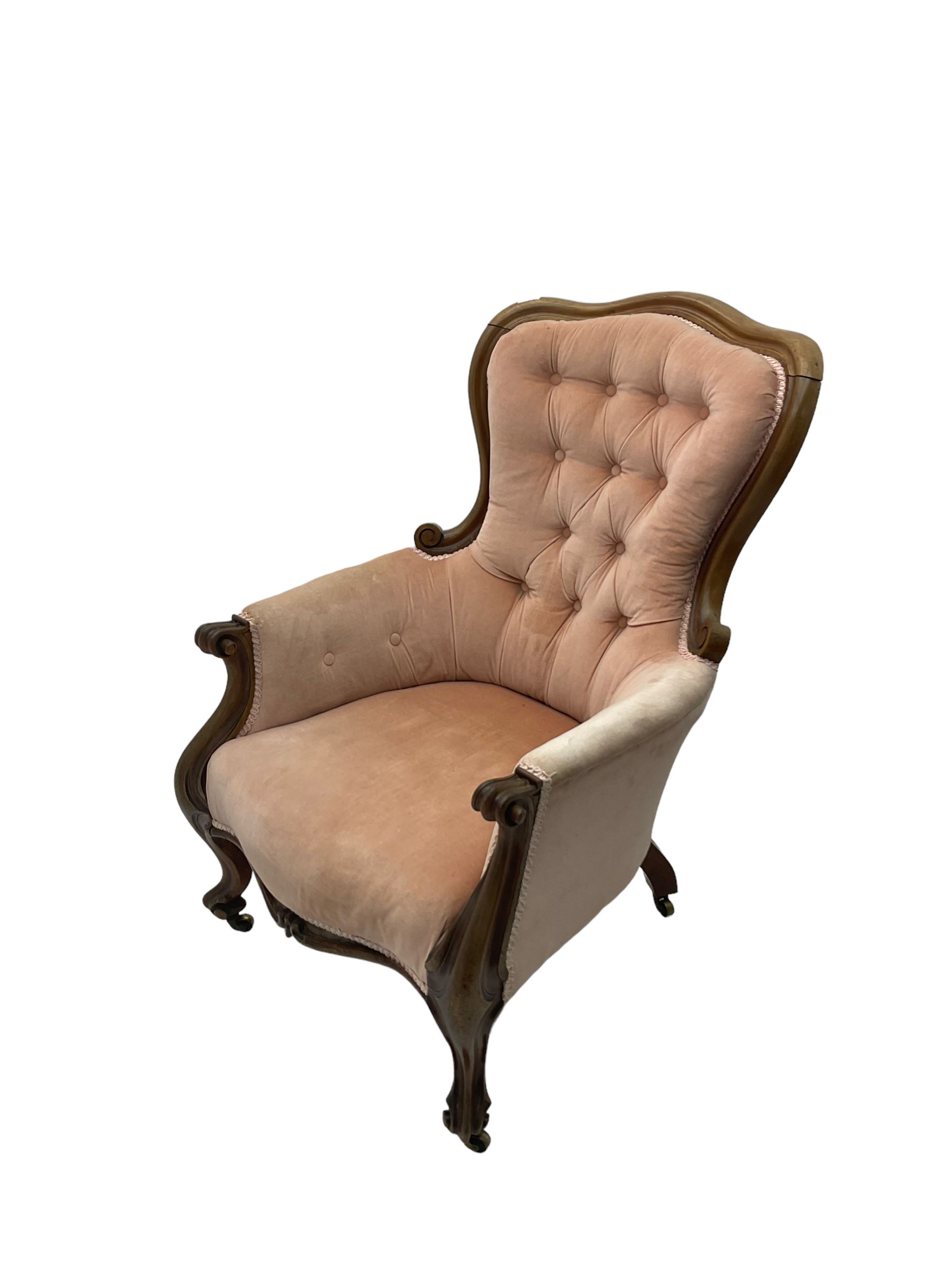 Victorian walnut framed armchair, shaped back with carved and scrolled arm terminals, upholstered in buttoned pale pink fabric, raised on cabriole supports terminating in castors