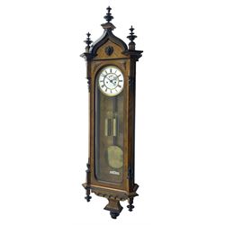 German - 19th century 8-day weight driven Vienna wall clock in a walnut and ebonised case, with an ogee arched pediment and ebonised finials, canted corners and fully glazed door, curved base with a carved arcade and pendants, two part porcelain dial with with a spun brass bezel, Roman numerals, pierced gothic hands and subsidiary seconds dial, rack striking movement with a dead-beat escapement and maintaining power, striking the hours and half hours on a coiled gong, visible ebony pendulum with a brass bob and two brass cased weights.