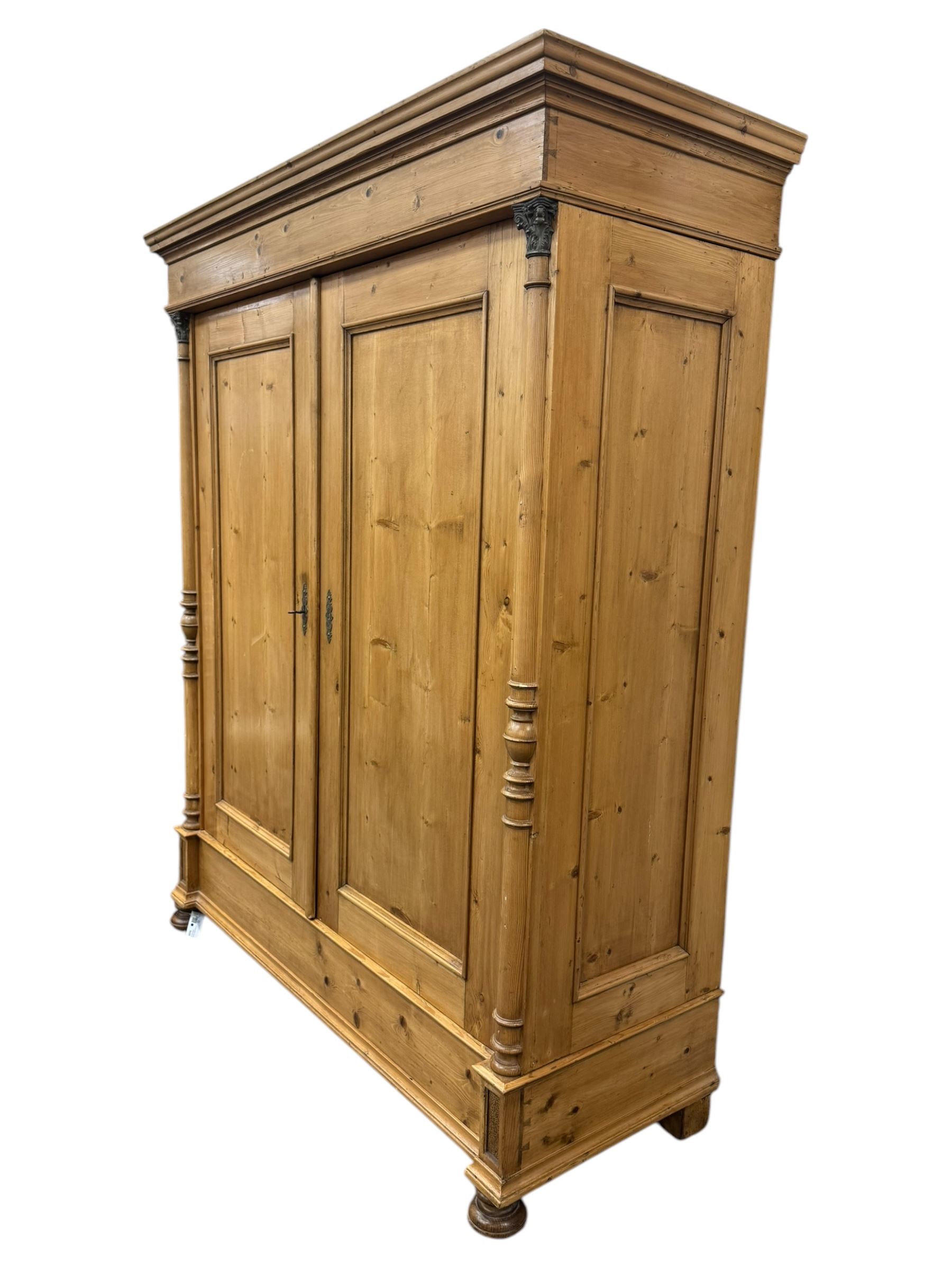 Large 19th-century Continental polished pine double wardrobe, panelled back and doors revealing brass hanging rod, flanked by half-turned columns with Corinthian capitals supported on bun feet