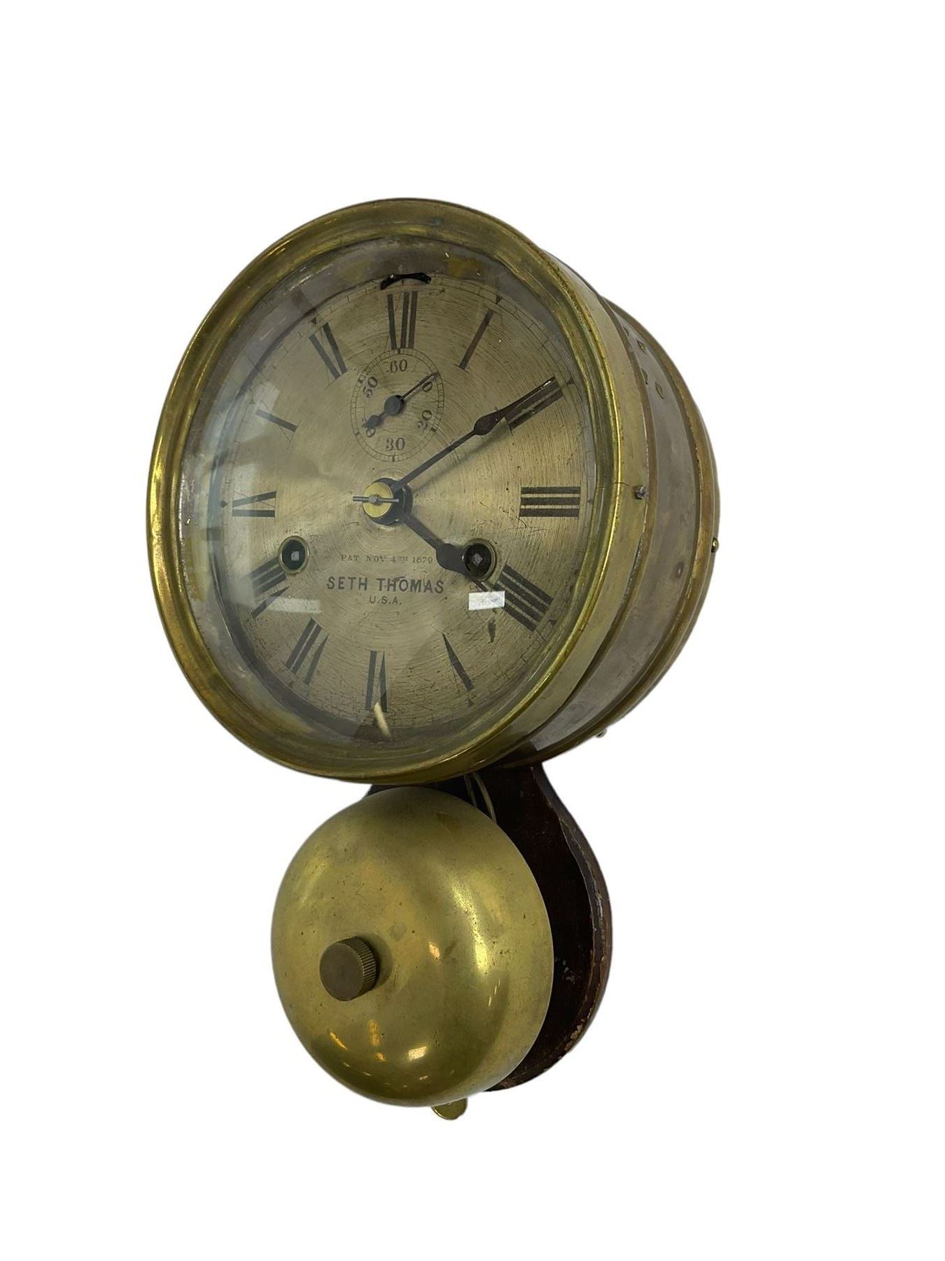 Seth Thomas U.S.A. Ships clock c1890, with a 6” silvered dial sounding the ships watch on a brass bell, eight-day twin train balance wheel movement, silvered dial with Roman numerals, steel spade hands, escapement regulation and subsidiary seconds dial, with a circular alloy drum case mounted on a wooden plaque, dial inscribed “4th November 4th 1879  Seth Thomas U.S.A.