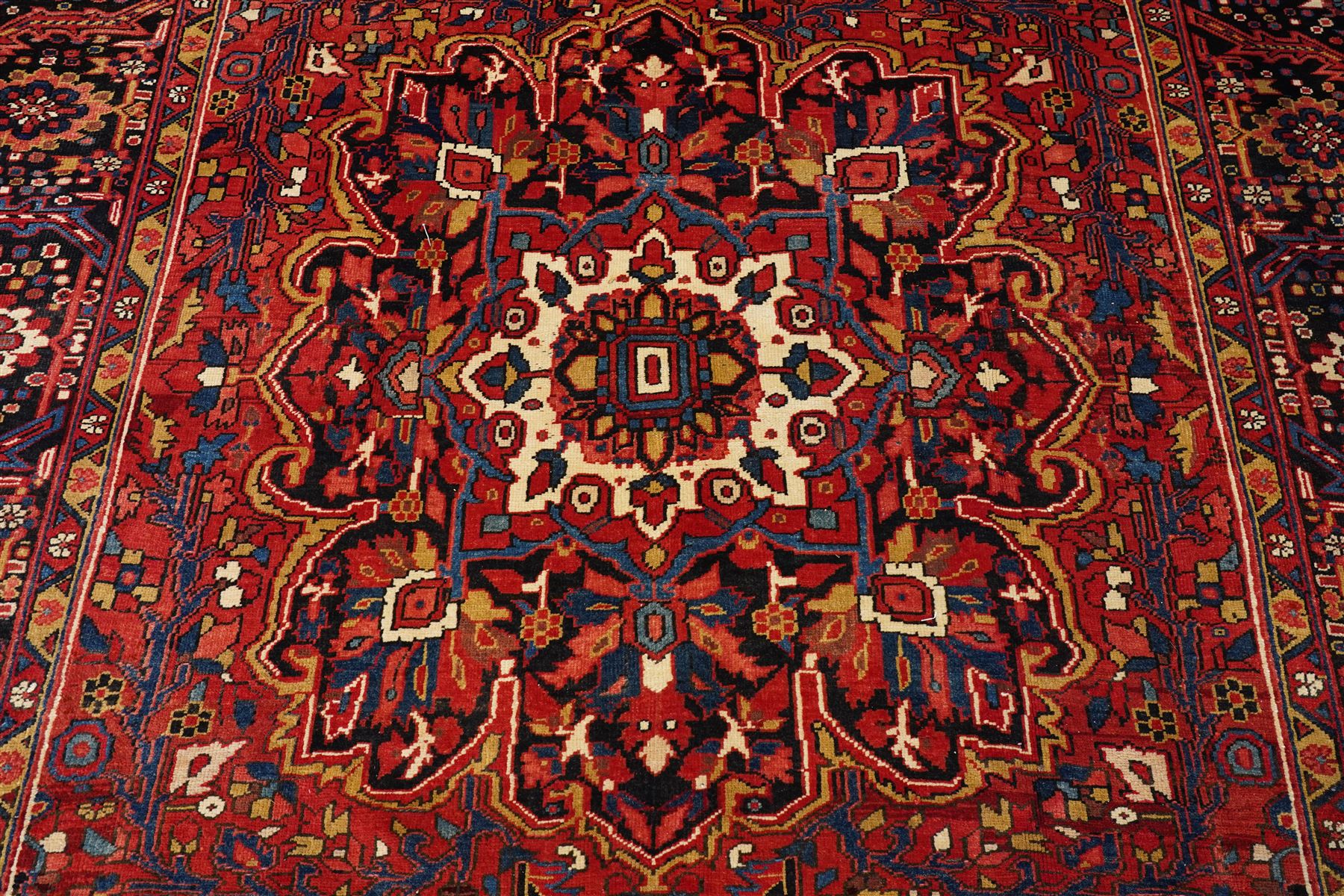 North West Persian Heriz/Ahar hand-knotted carpet, brick-red field with a large central angular stepped medallion with pendant motifs, surrounded by stylized palmettes, serrated leaves and geometric floral devices , ivory corner spandrels, enclosed by a dark indigo main border of stylized rosettes and angular vine motifs, between multiple guard stripes, with cotton fringe ends 