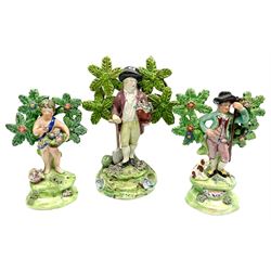 Three early 19th century Staffordshire John Walton figures, the largest example modelled as a gardener with urn of flowers in one arm, leaning against a shovel, the other two examples modelled as a Shepherd with dog at feet, and young boy with basket of flowers in one arm, each with bocage support, and inscribed 'Walton' verso, largest example H17.5cm, smaller examples approximately H14cm 