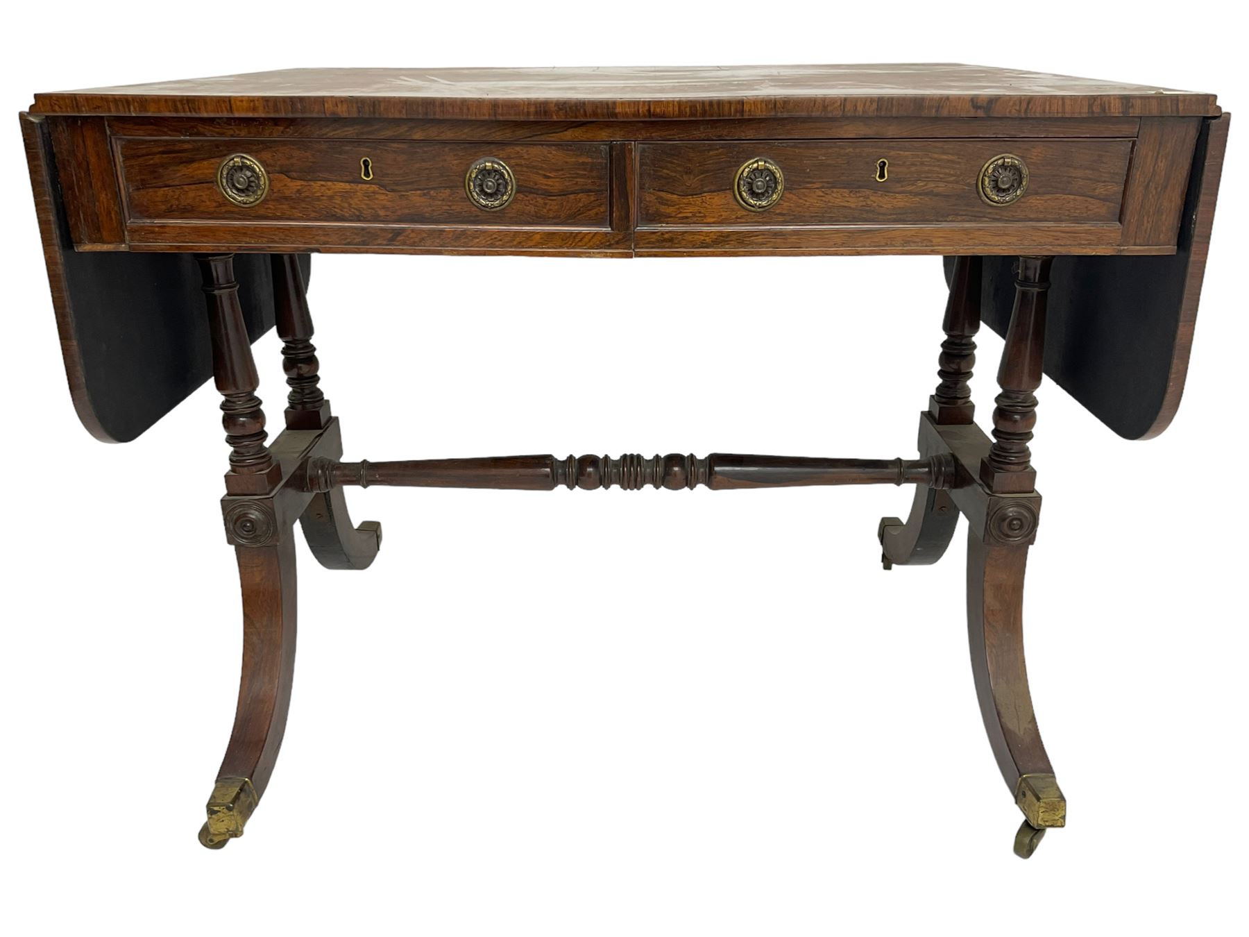 Regency rosewood sofa table, drop leaf rectangular top with rounded corners, fitted with two drawers and two opposing false drawers, raised on dual turned columns terminating in splayed feet united by turned stretcher, on brass cups and castors