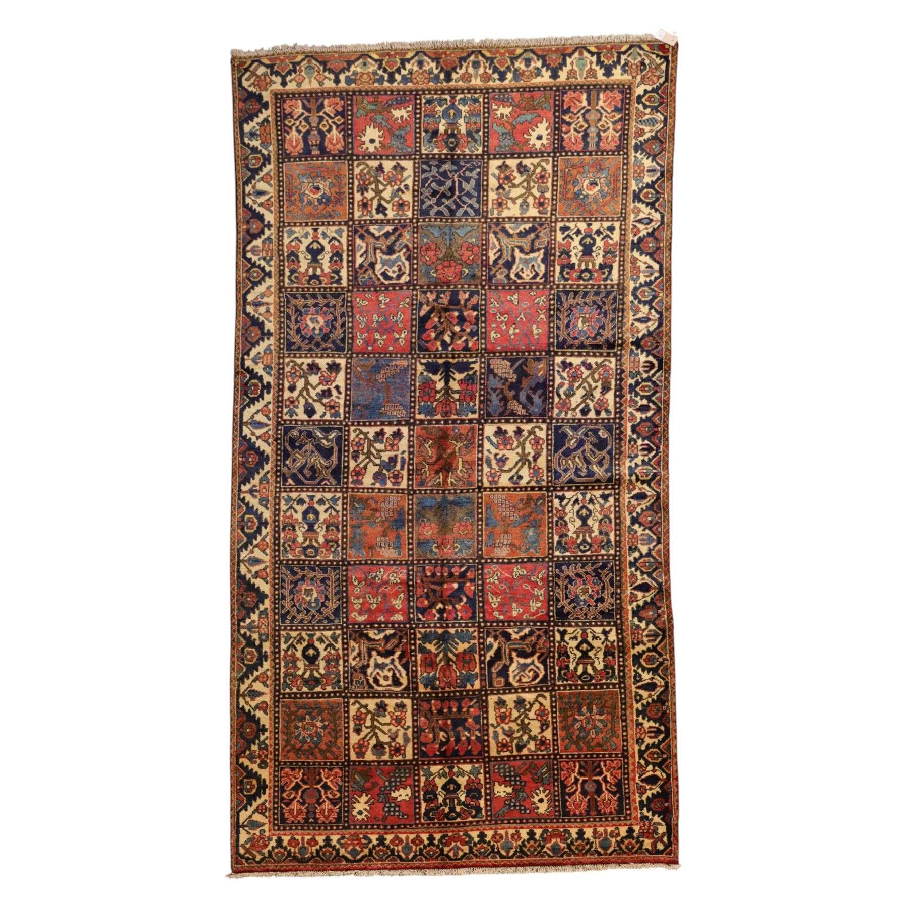 Central Persian Bakhtiari Kheshti design hand-knotted rug, field composed of a grid of square panels, each containing stylized floral devices, animal and foliate motifs woven in a rich palette of madder red, indigo blue, ivory ochre and brown, framed by a multiple striped border with a meandering vine and flowerhead band, with cotton fringe ends 