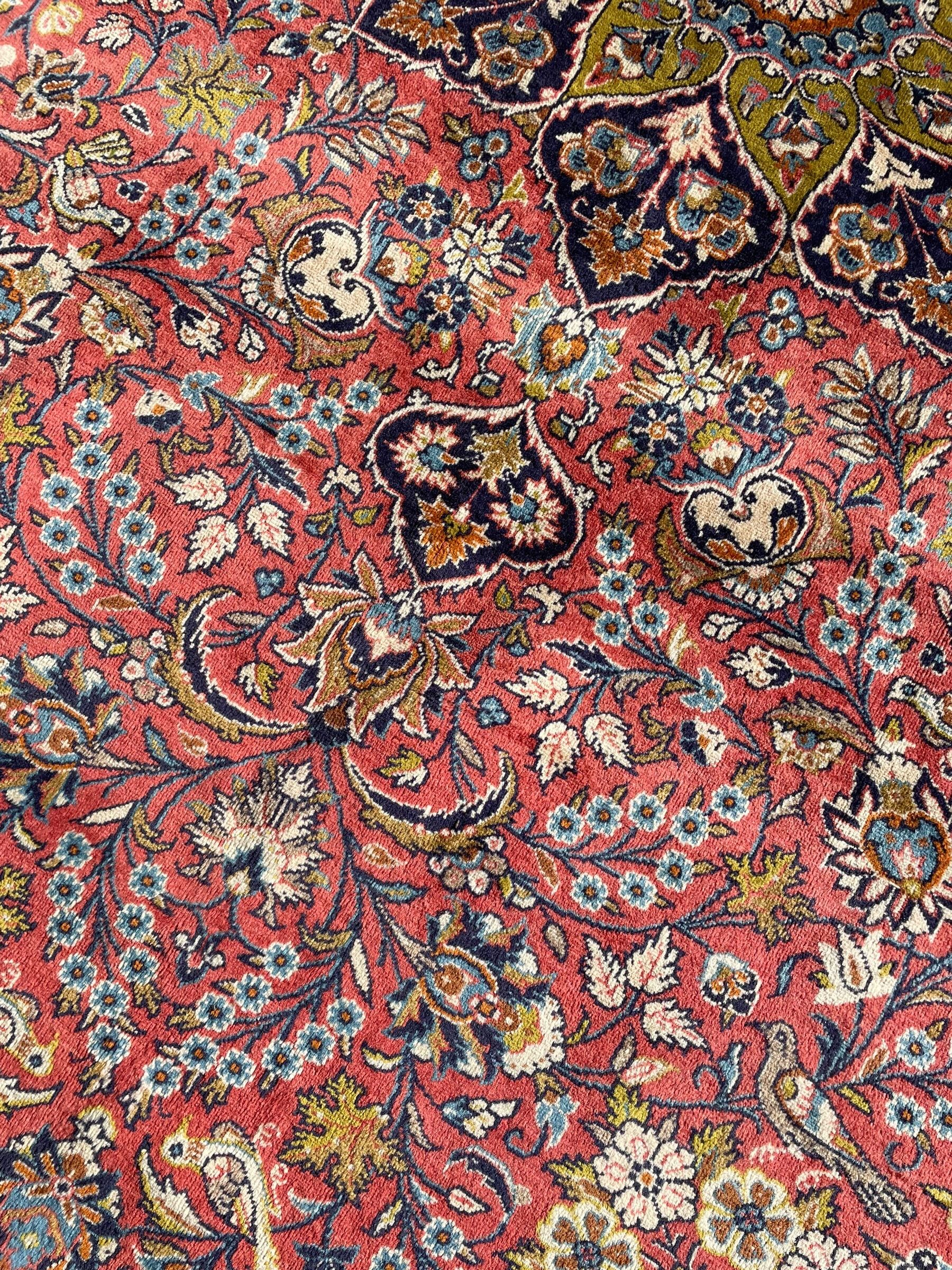 Persian Kashan peach ground rug, central rosette medallion surrounded by trailing branches and flower heads with bird motifs, light blue spandrels with further floral decoration, the main border with repeating palmettes and birds, within guard stripes