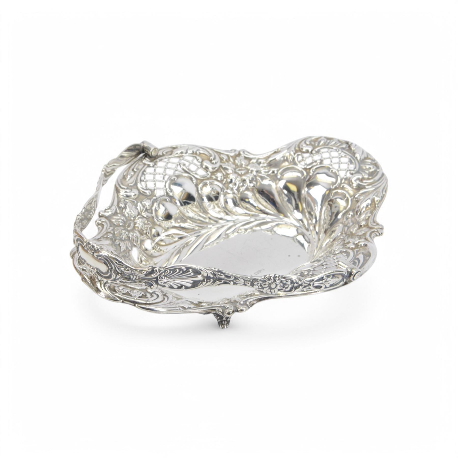Edwardian silver swing handled basket, of oval form with shaped rim, embossed with floral decoration and with pierced latticework sides, upon four pad feet, hallmarked Chester 1905, maker's mark worn and indistinct