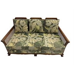 Early 20th century bergère lounge suite, mahogany framed with cane work back and sides, acanthus scroll carved uprights - three seat sofa (W167cm, H82cm, D83cm), and pair matching armchairs (W78cm), loose cushions upholstered in acanthus leaf scroll fabric with scatter cushions