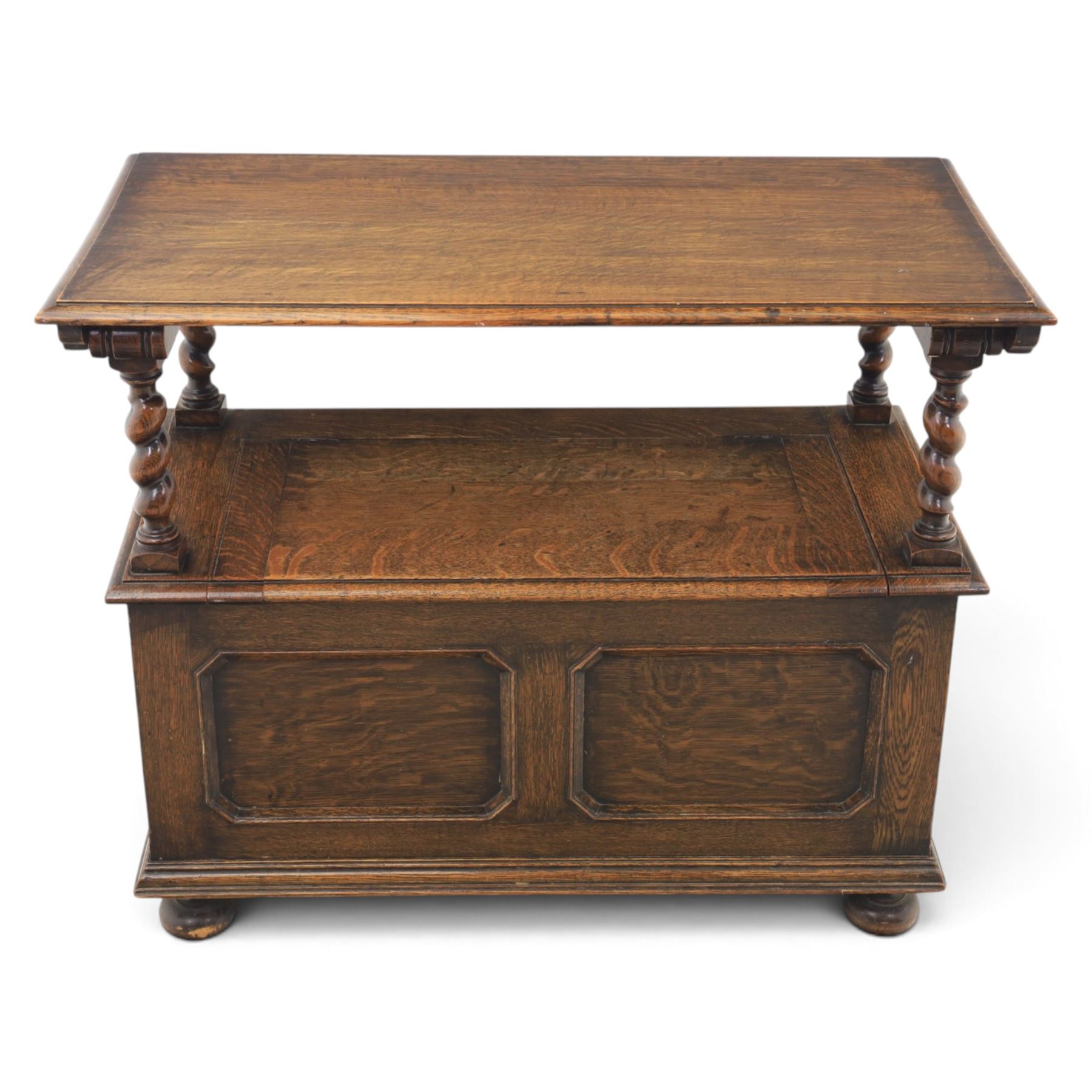Early 20th century oak monks bench, panelled back converting to a table top, reeded armrests with barley twist uprights, hinged seat over panelled base supported on bun feet