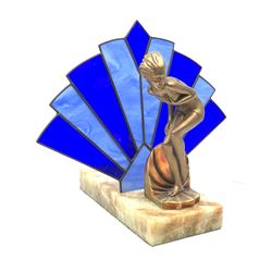 An Art Deco style table lamp, modelled in the form of a bronzed female figure before a leaded blue glass fan shaped shade, upon rectangular onyx base, overall H32cm base L28cm. 