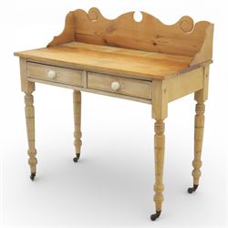 19th century stripped pine side table, the rectangular plank top with low shaped back rail incorporating scroll cut ends, fitted with two frieze drawers with ceramic knob handles, raised on turned supports terminating in castors