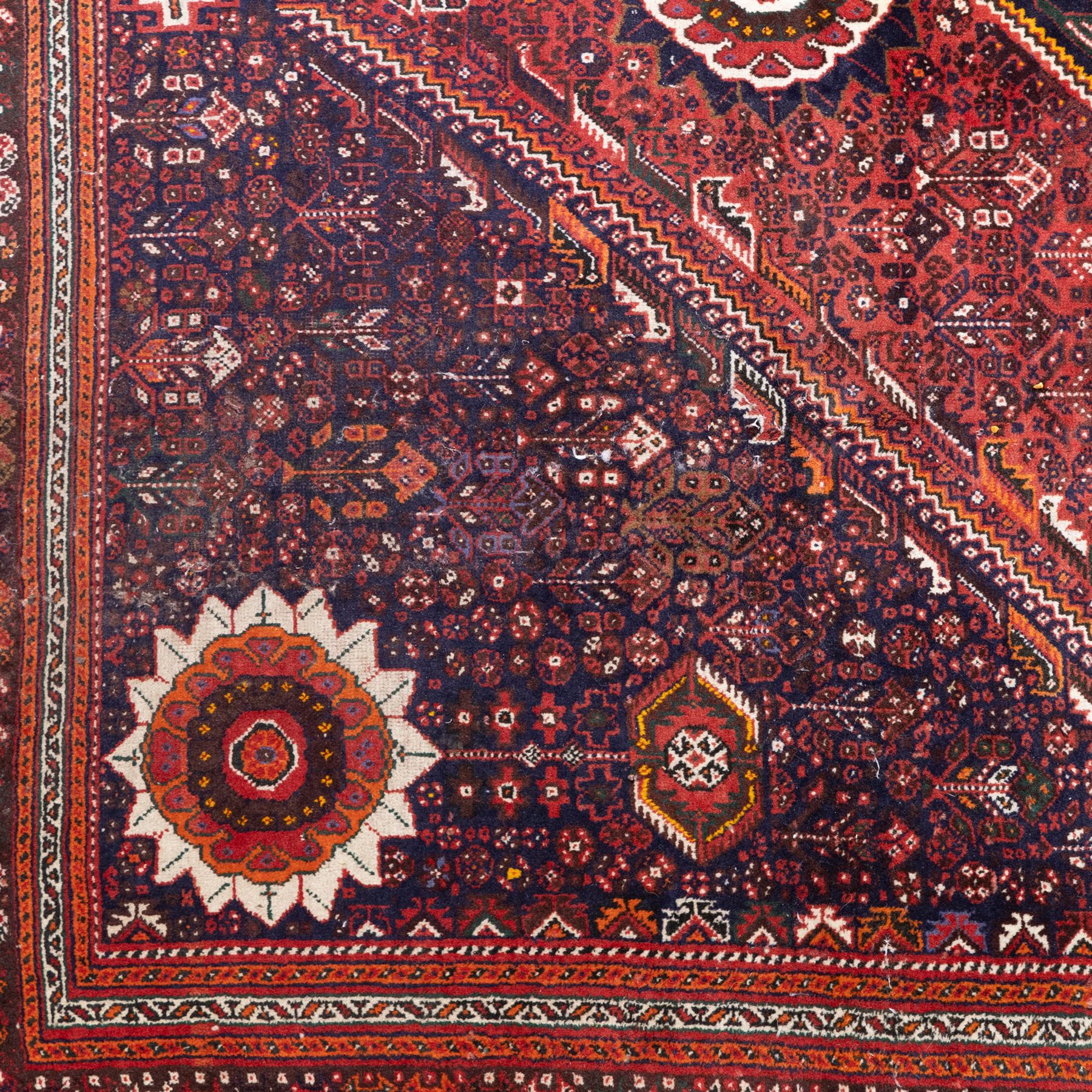 Qashqai wool carpet, red diamond-shaped field decorated with three stepped pole medallions, floral rosettes and scattered stylised motifs, within dark blue spandrels and multiple geometric guard borders