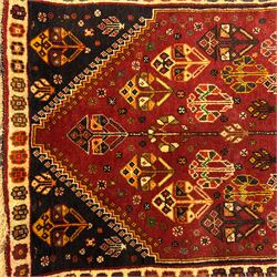 South West Persian Qashqai rug, hand knotted wool with central dark blue lozenge medallion containing geometric motifs, on a madder red field decorated with stylised floral boteh motifs, indigo spandrels, multiple borders of floral rosettes, from the region of Fars, south-west Persia