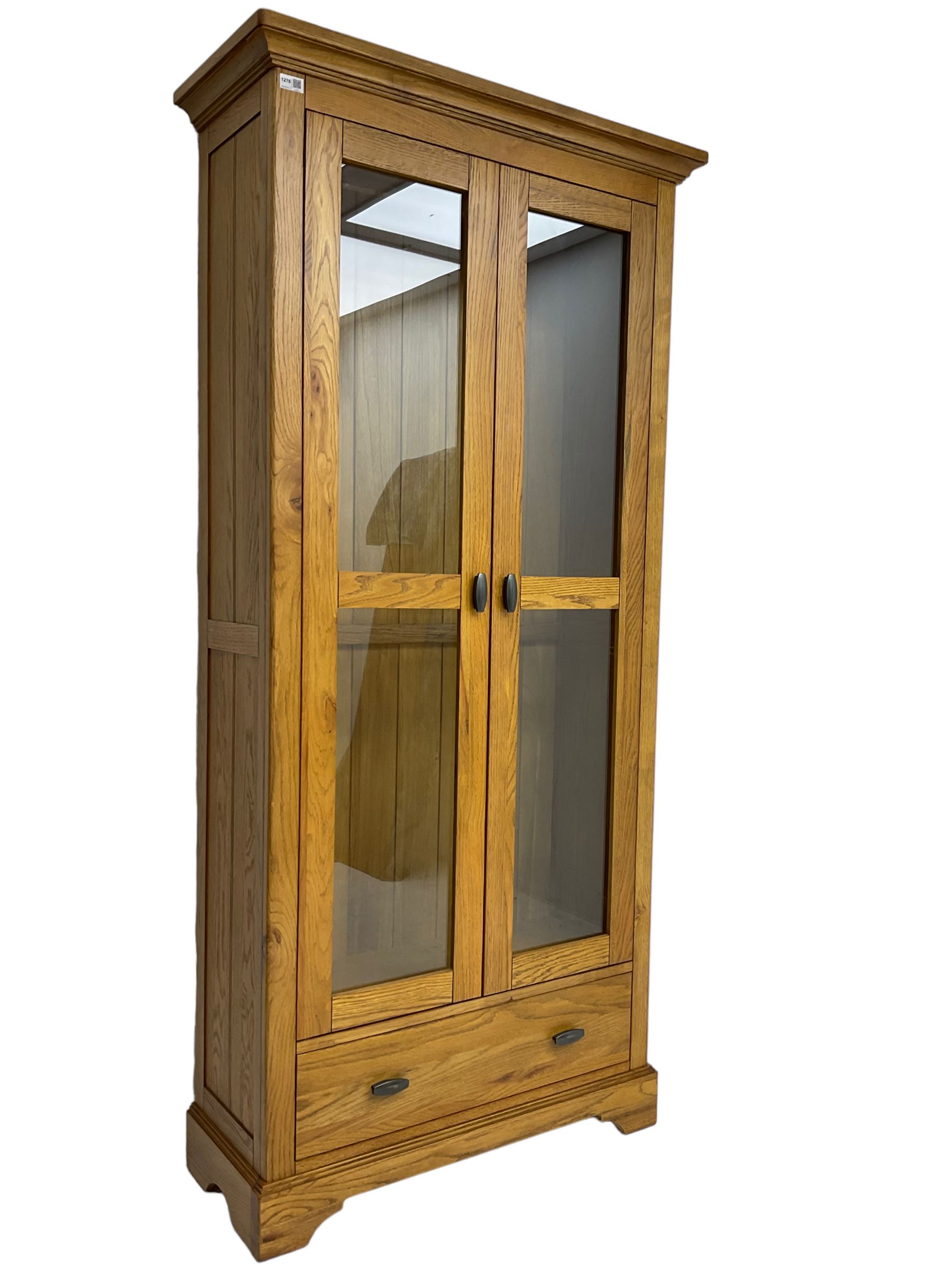 Tall oak display cabinet, projecting cavetto cornice over two glazed doors and single drawer, on bracket feet