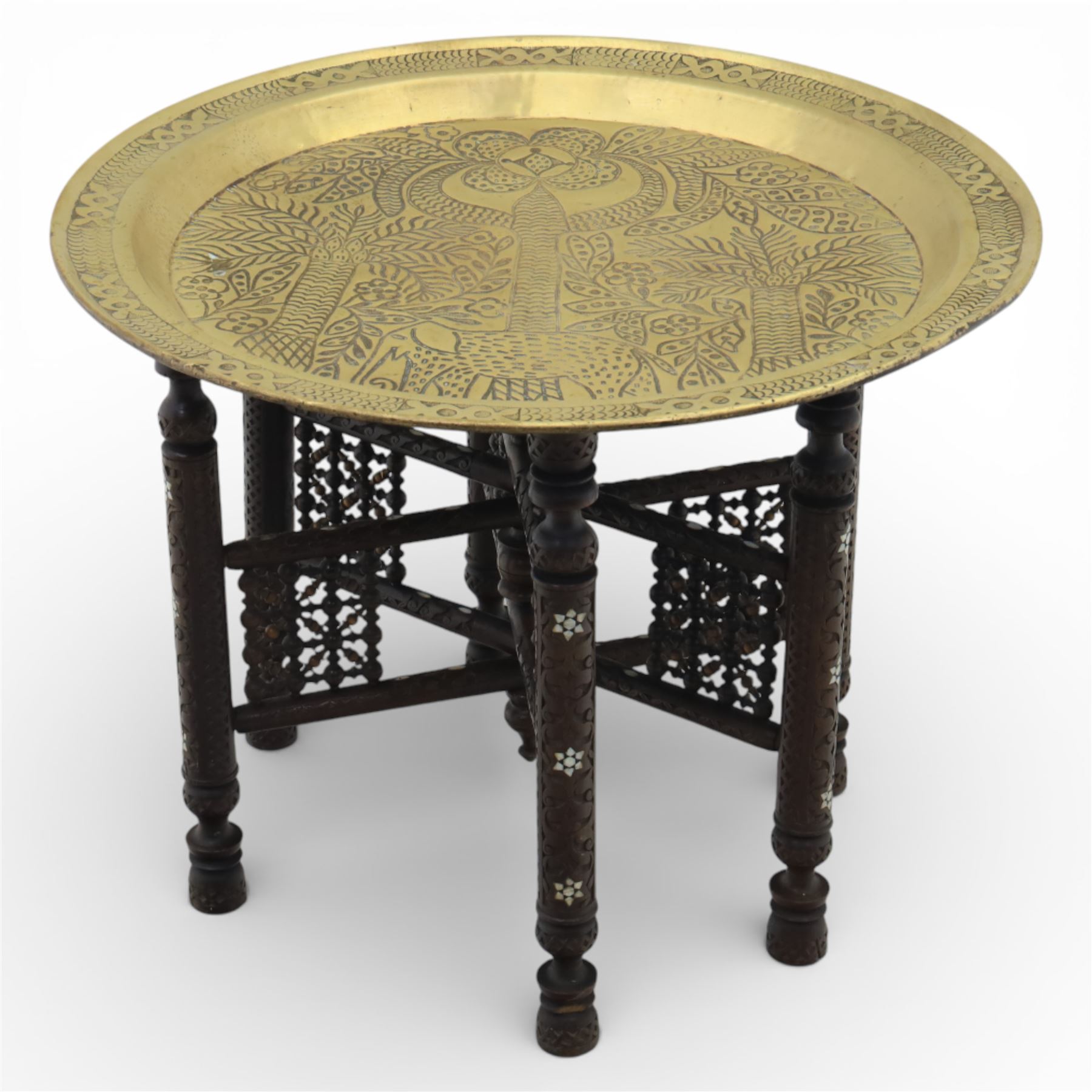 20th century Eastern brass charger topped table, the circular brass trap chased with an elephant, palm tress and flowering vines, supported upon a folding stand with six turned legs with inlaid detail, united by turned supports