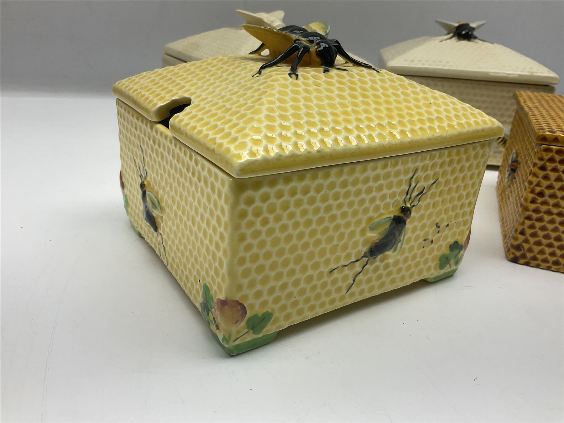 Four square honey boxes with lids,  each decorated with honeycomb pattern and finished with a bee finial