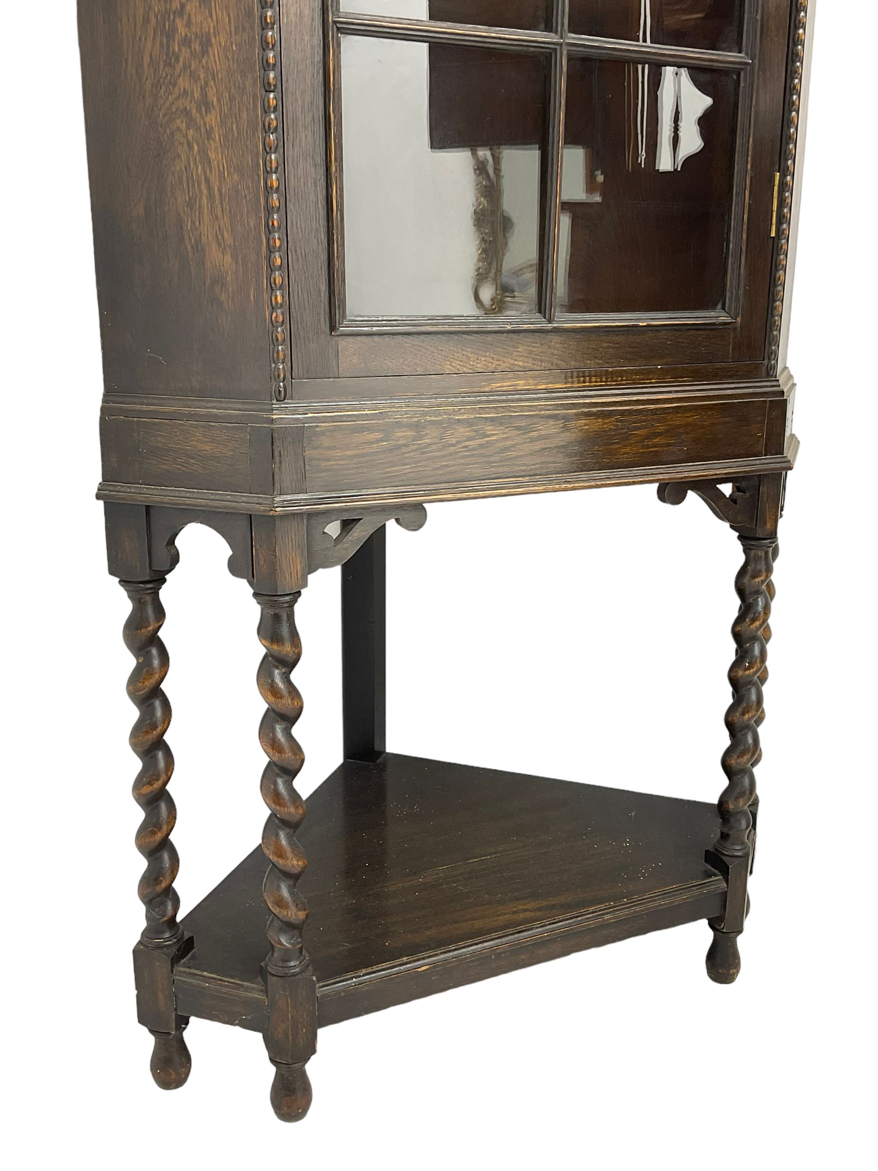 Early 20th century oak corner display cabinet, enclosed by glazed door, on spiral turned supports joined by undertier 