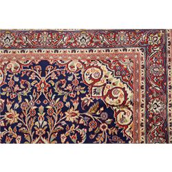 Central Persian Kashan hand-knotted rug, indigo field with central lobed medallion with pendants issuing scrolling arabesque of palmettes, flowering vines, and foliate tendrils, with conforming spandrels, with vine border and framed by guard stripes in tones indigo, ivory and madder red, with cotton fringe ends 