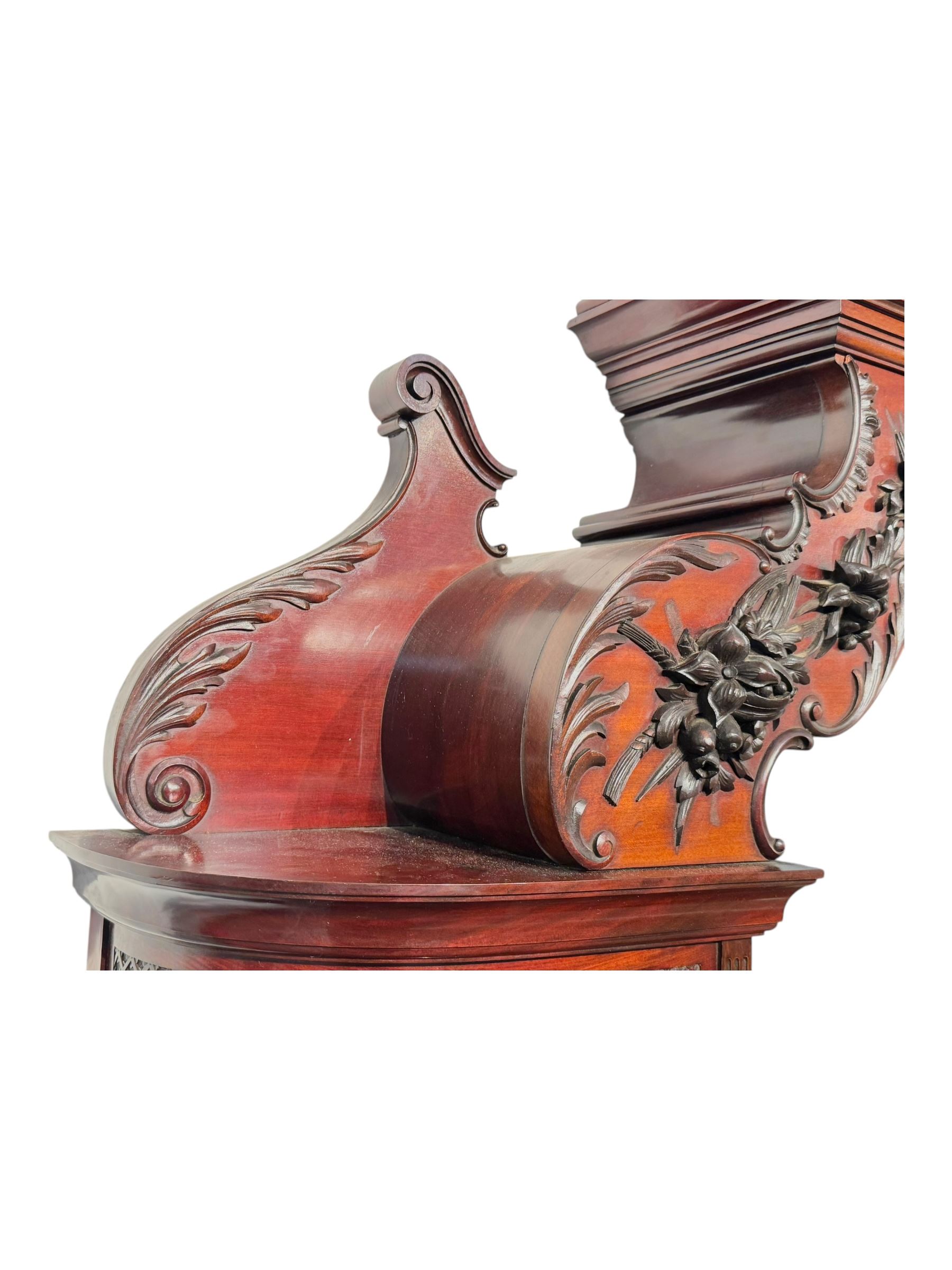 Late 19th century mahogany mirror back cabinet, shaped C-scroll pediment decorated with carved acanthus leaf cartouche and shells, shaped canopy top with applied foliate carvings over triple bevelled mirror back, central cupboard enclosed by panelled door carved with musical instruments, scrolls and shells, flanked by two glazed cabinets, on acanthus leaf carved cabriole supports united by undertier 